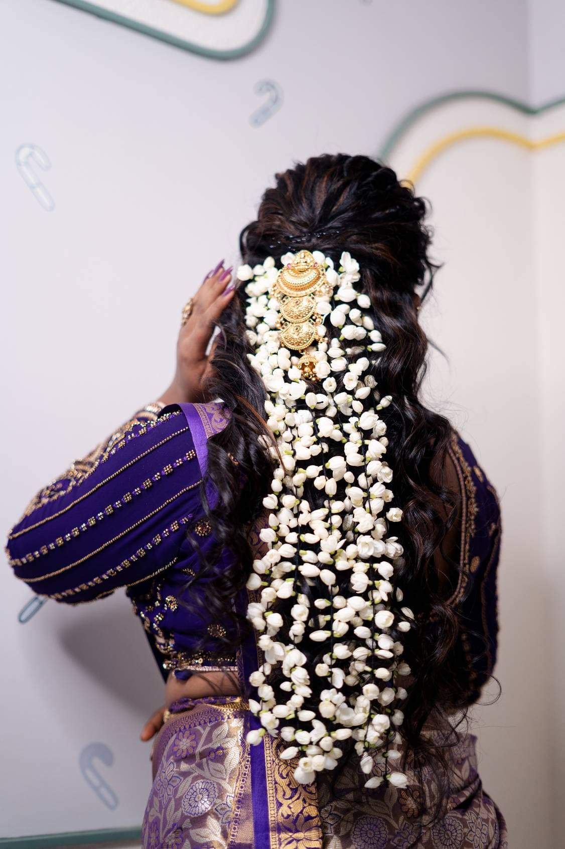 Bridal hairstyle with loose curls and a jasmine flower gajra worn with a purple and gold silk saree, styled at Page 3 Luxury Salon, Madurai